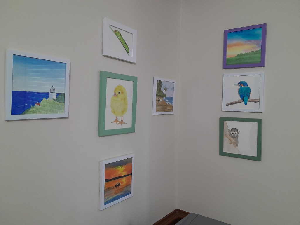 Corner of a room with various watercolor paintings hung on the walls.