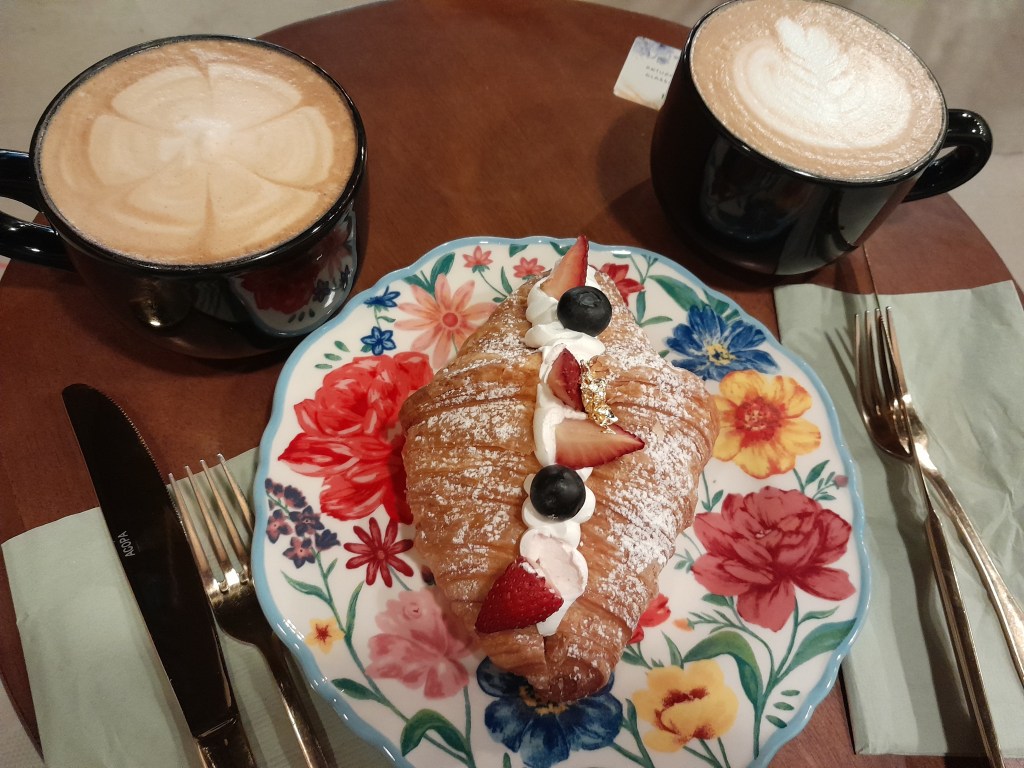 Decorative plate with strawberry croissant and two coffees with coffee art.